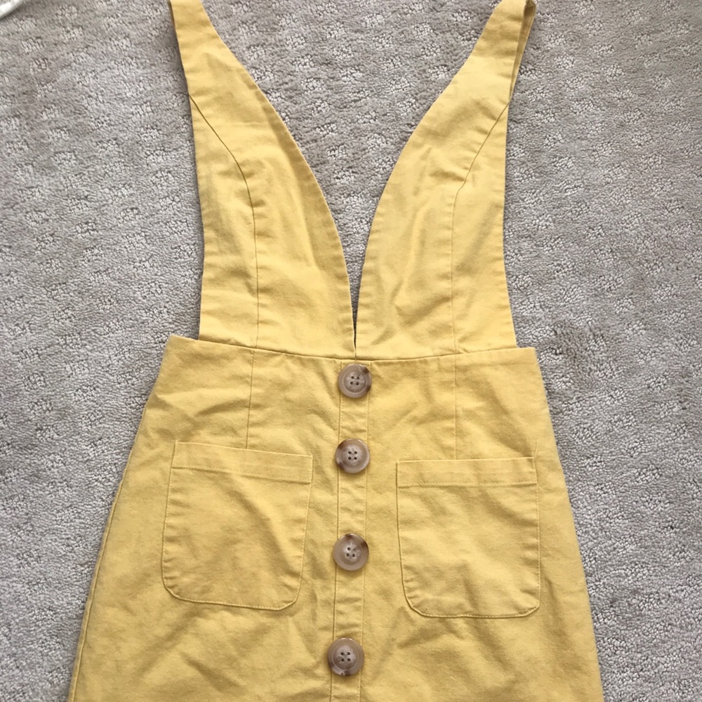 a yellow overall dress with brown buttons
